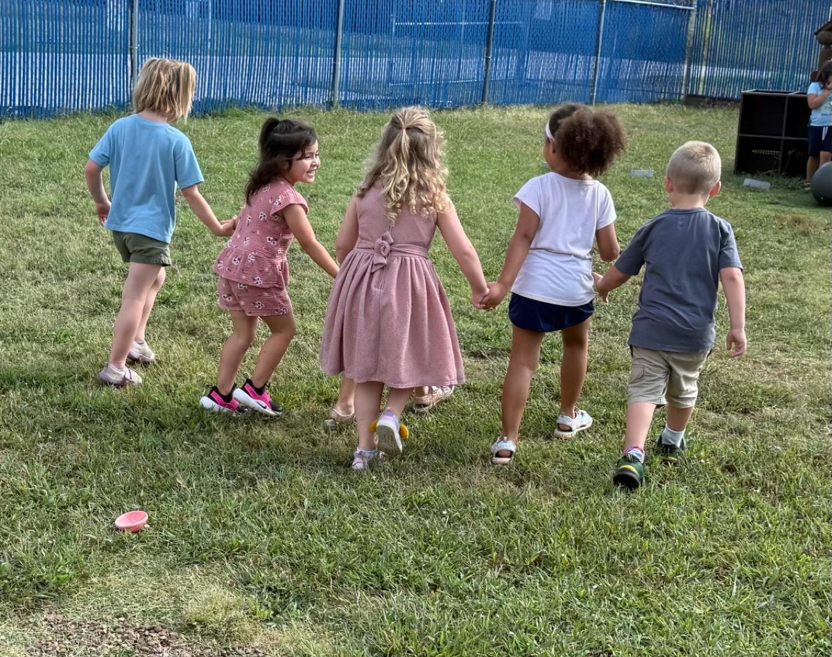 Children holding hands as they play outside on the grass